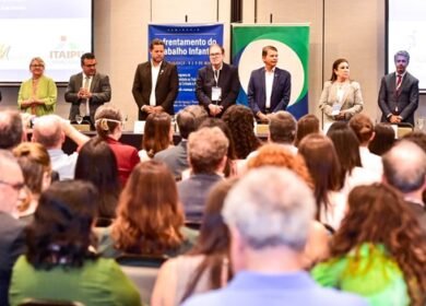 Fotografia de nove pessoas em pé, duas mulheres e sete homens, em frente a uma plateia no seminário de combate ao trabalho infantil