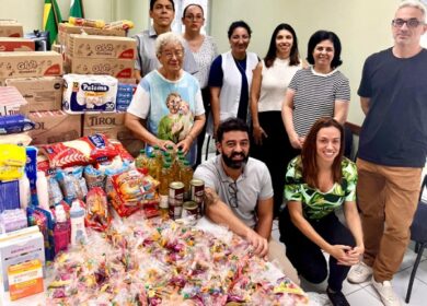 Registro de um grupo de nove pessoas ao lado de uma mesa cheia de donativos arrecadados.
